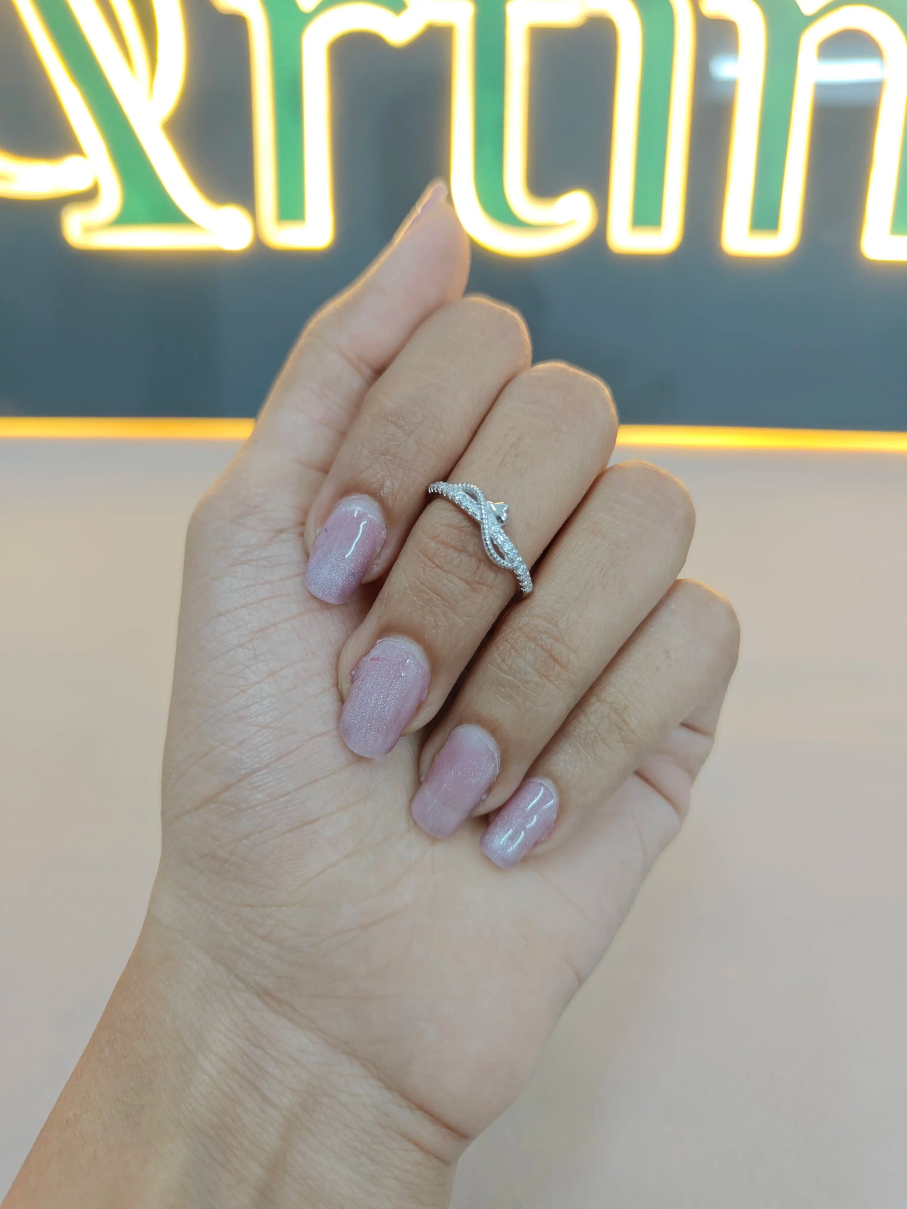 Hand with a diamond ring against a blurred neon sign background
